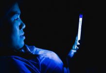 person sat with their phone in the dark emitting a harsh blue light