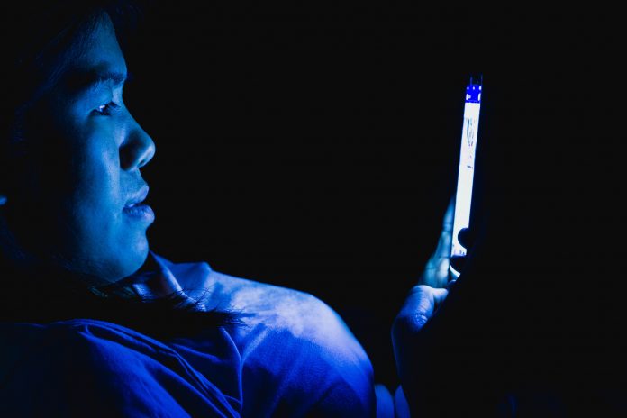 person sat with their phone in the dark emitting a harsh blue light