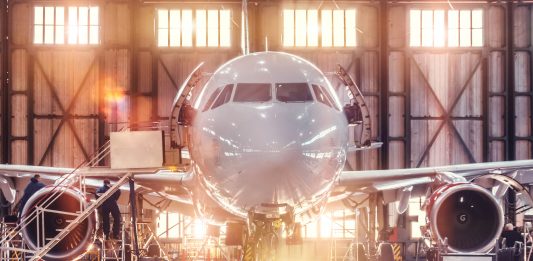Airplane under repair in the aerospace hangar in the background of the gate and bright sunlight