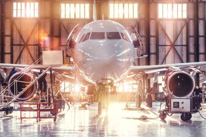 Airplane under repair in the aerospace hangar in the background of the gate and bright sunlight