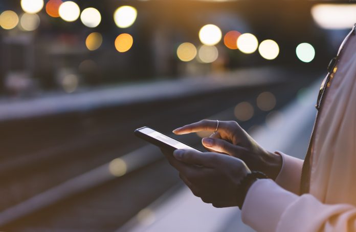 Woman waits by train platform as she checks her phone