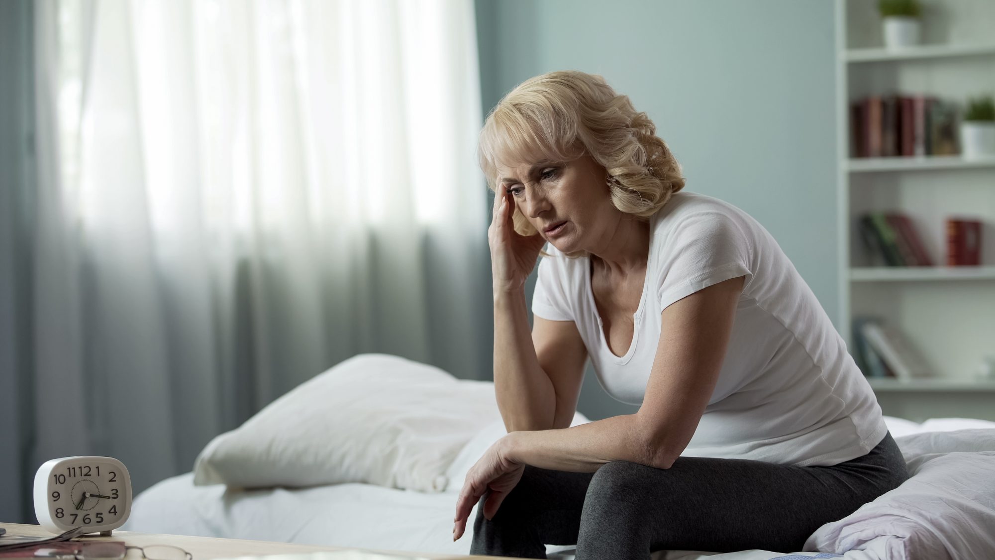 Middle aged woman sat on her bed going through menopause looking stressed and tired