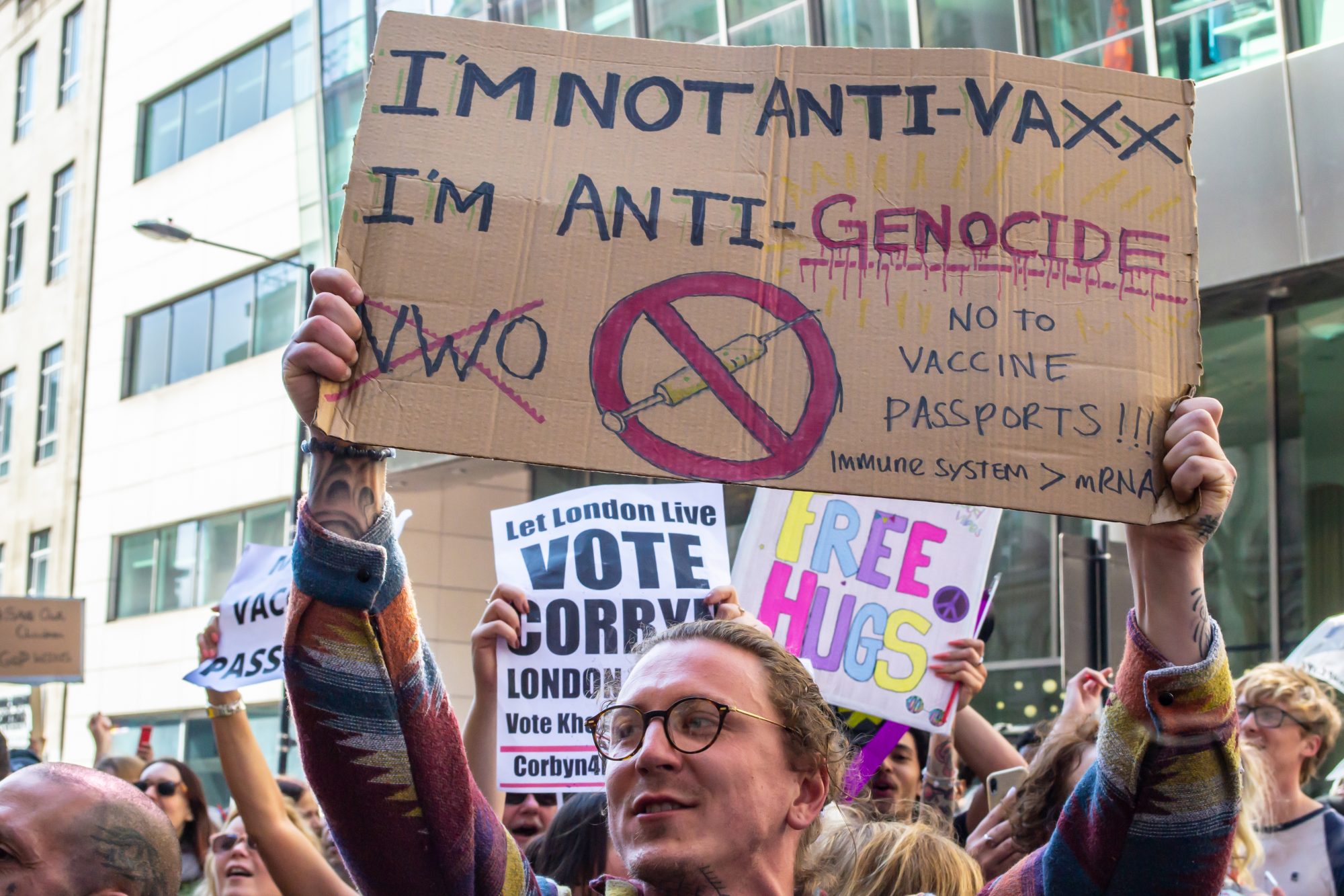 Anti-vaccine protestor holds sign reading 'I'M NOT ANTI-VAXX I'M ANTI-GENOCIDE'