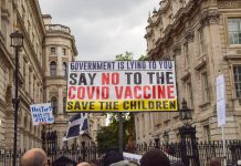 Antivaxxers holding sign at protest reading 'GOVERNMENT IS LYING TO YOU SAY NO TO THE VACCINE SAVE THE CHILDREN'