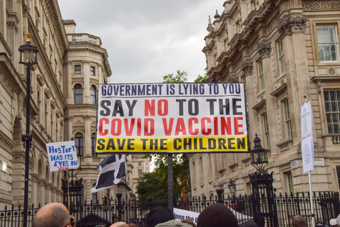 Antivaxxers holding sign at protest reading 'GOVERNMENT IS LYING TO YOU SAY NO TO THE VACCINE SAVE THE CHILDREN'