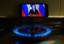 Phone showing Putin on screen propped up by gas stove