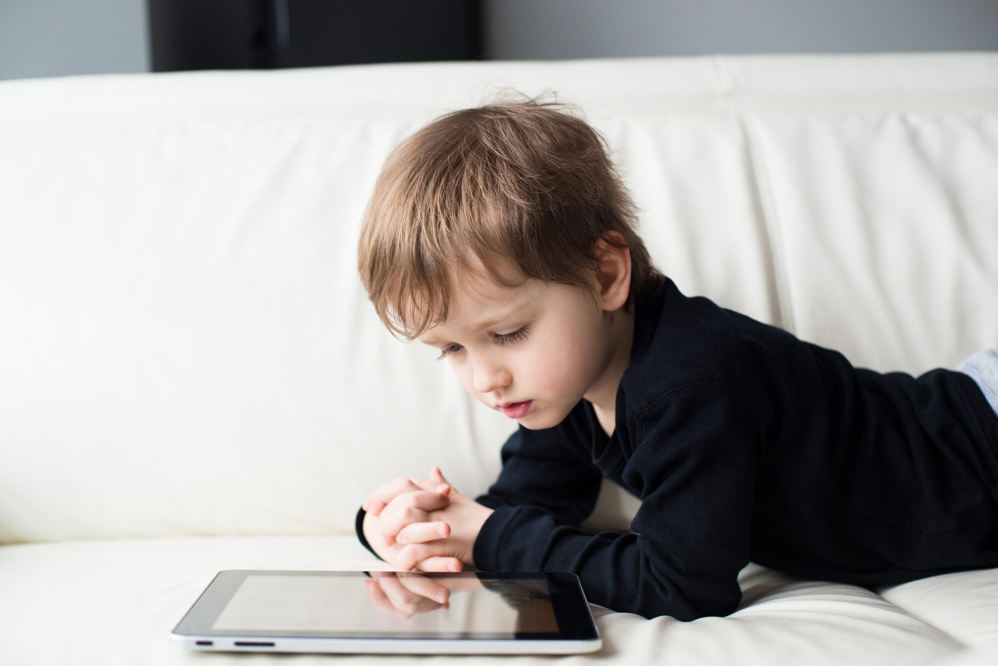 Small boy uses tablet on sofa