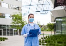 NHS worker wearing personal protective equipment holding folder standing in front of hospital