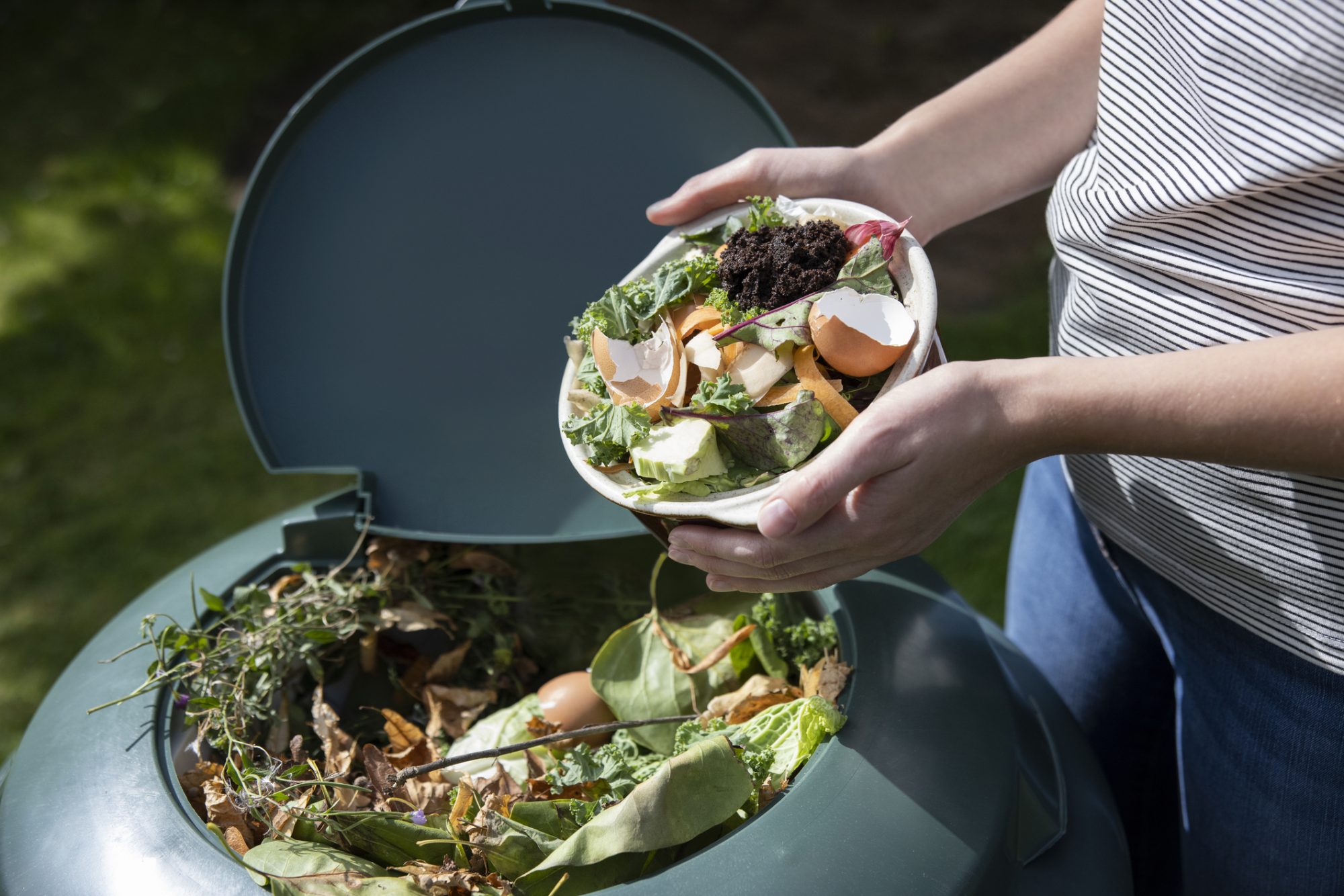 Close Up Of Woman Emptying Food Waste Into Garden Composter At Home