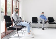 Young and mature man with face masks sitting in a waiting room of a hospital or office