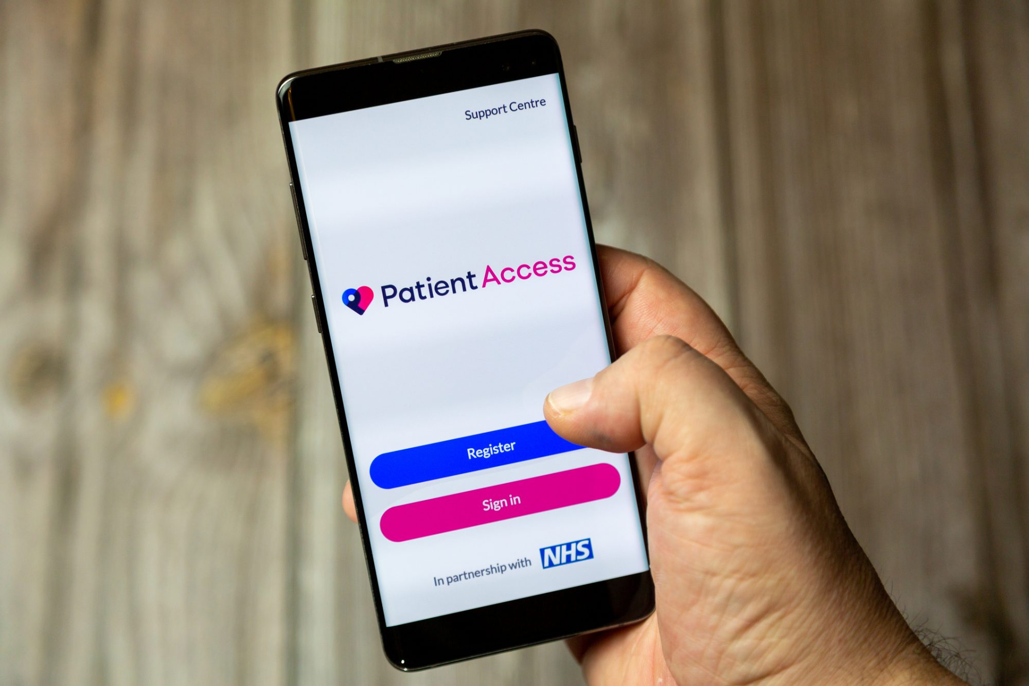 A mobile phone or cell phone being held by a hand with the Patient Access app by NHS open on screen 
