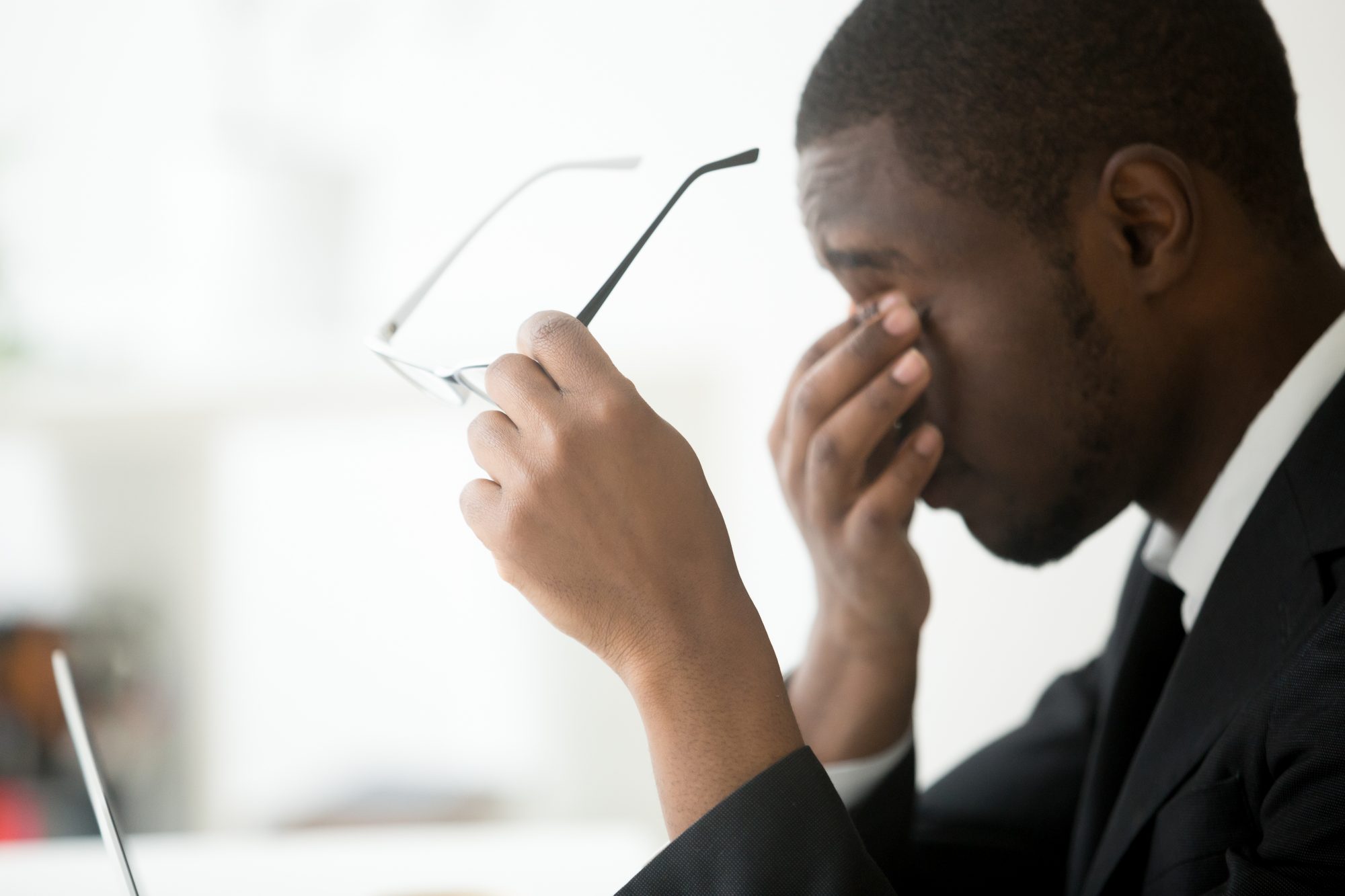 Young black male in suit holding hand to his face due to fatigue 