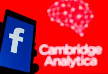 Person holding phone with Facebook app on screen in front of a red background reading 'Cambridge Analytica'