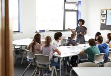 Female High School Tutor Standing By Table With Students Teaching Lesson