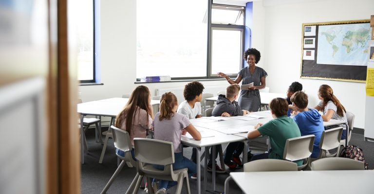 Female High School Tutor Standing By Table With Students Teaching Lesson