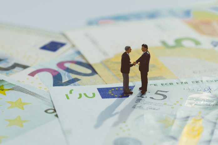 Brexit agreement, Europe and UK economy deal, financial, investment or currency exchange concept, miniature businessman figurine hand shaking and looking at stars on pile of Euro banknotes