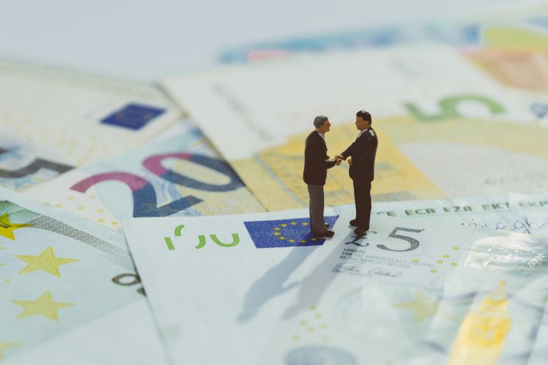 Brexit agreement, Europe and UK economy deal, financial, investment or currency exchange concept, miniature businessman figurine hand shaking and looking at stars on pile of Euro banknotes