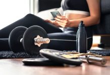 Woman in exercise gear sitting on floor behind weights using health app to guide her workout.