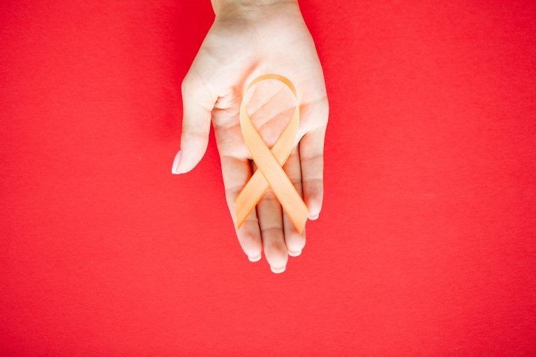 Close up of a doctor holding and showing orange awareness ribbon in her hands