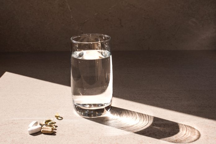 Vitamin D supplements and glass of water sitting on table in sunlight