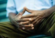 Older black man sitting on park bench with fingers intertwined, feeling pensive