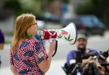 Woman wearing American flag shirt speaks into megaphone decorated with cannabis plant leaves