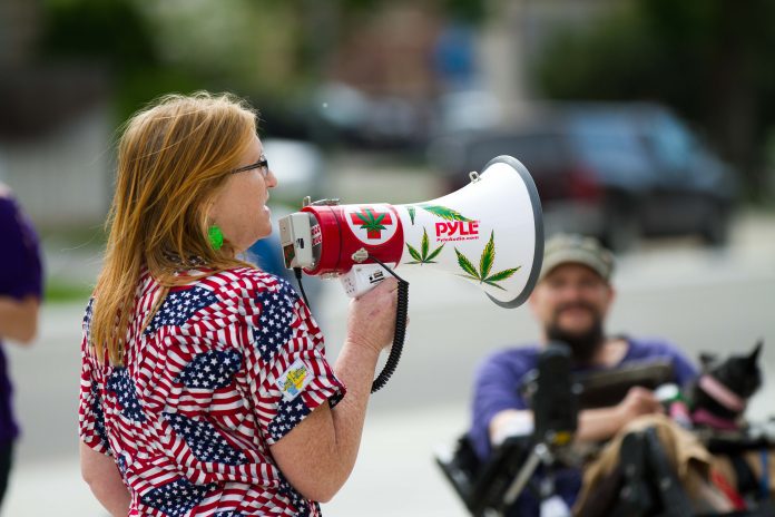 Woman wearing American flag shirt speaks into megaphone decorated with cannabis plant leaves