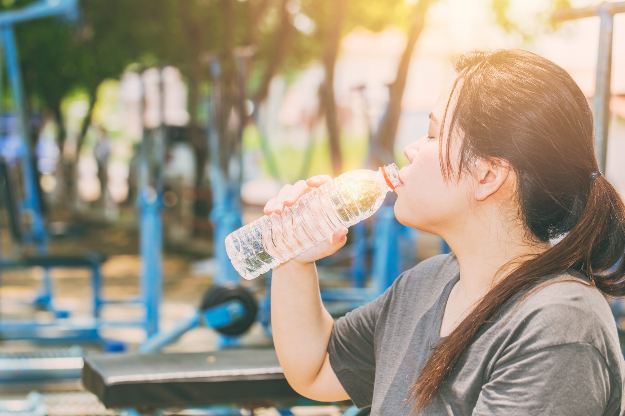 Asian woman with ponytail drinking water in front of row of treadmills in gym