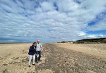 Man and woman looking down at ancient footprints on beach in Formby