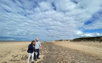 Man and woman looking down at ancient footprints on beach in Formby