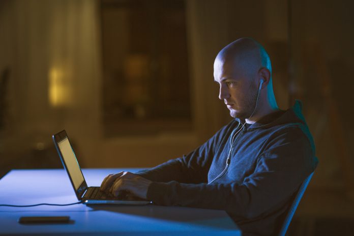 White male hacker sitting in dark room listening into people's calls