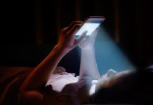 Young woman on phone in bed, blue light contributing to aging process