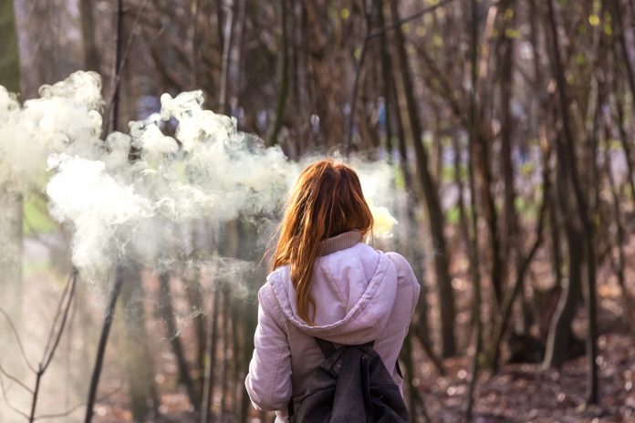Young school girl vaping in wooded area