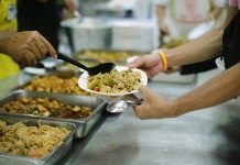 Food bank/food shelter. Volunteer handing over bowl of hot food to person in canteen