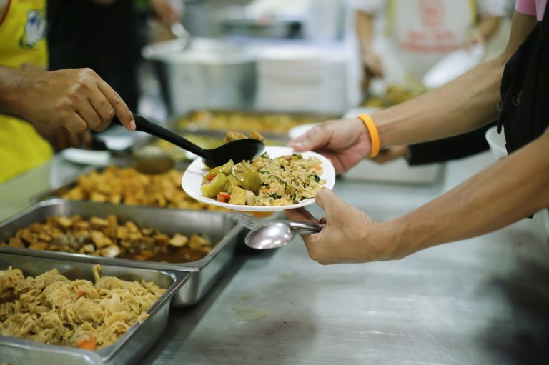 Food bank/food shelter. Volunteer handing over bowl of hot food to person in canteen