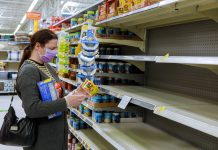 Woman wearing face mask shopping for groceries in US supermarket amidst the cost of living crisis, some empty shelves due to supply issues