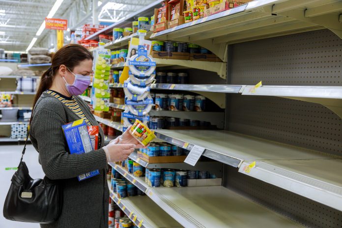 Woman wearing face mask shopping for groceries in US supermarket amidst the cost of living crisis, some empty shelves due to supply issues