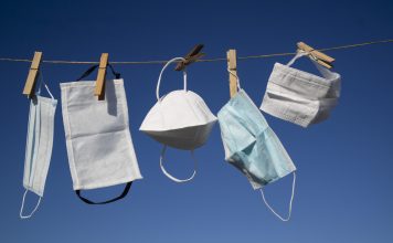 Various types of Covid masks hanging to dry/air out on washing line against a clear blue sky