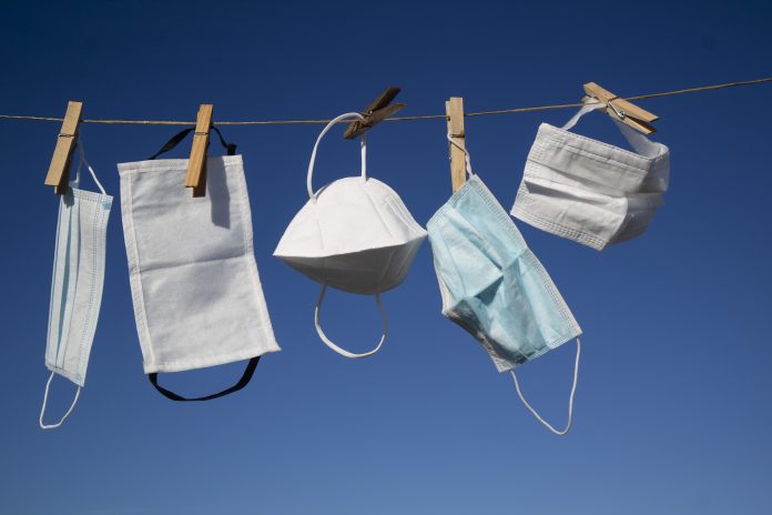 Various types of Covid masks hanging to dry/air out on washing line against a clear blue sky