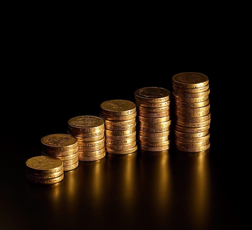 Black background with stack of British pound coins in varying amounts