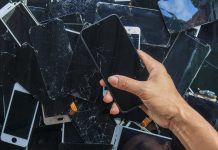 Person holding smartphone above pile of damaged smartphones