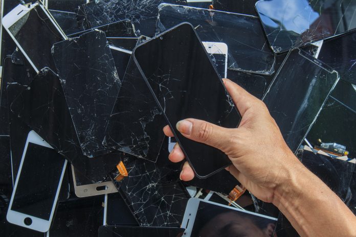 Person holding smartphone above pile of damaged smartphones