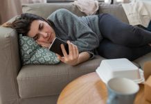 Anxious, depressed woman lying on sofa 'doomscrolling' on mobile phone