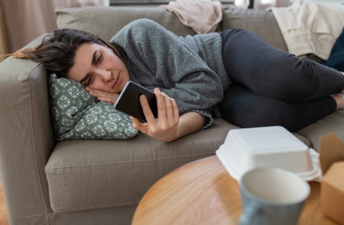 Anxious, depressed woman lying on sofa 'doomscrolling' on mobile phone