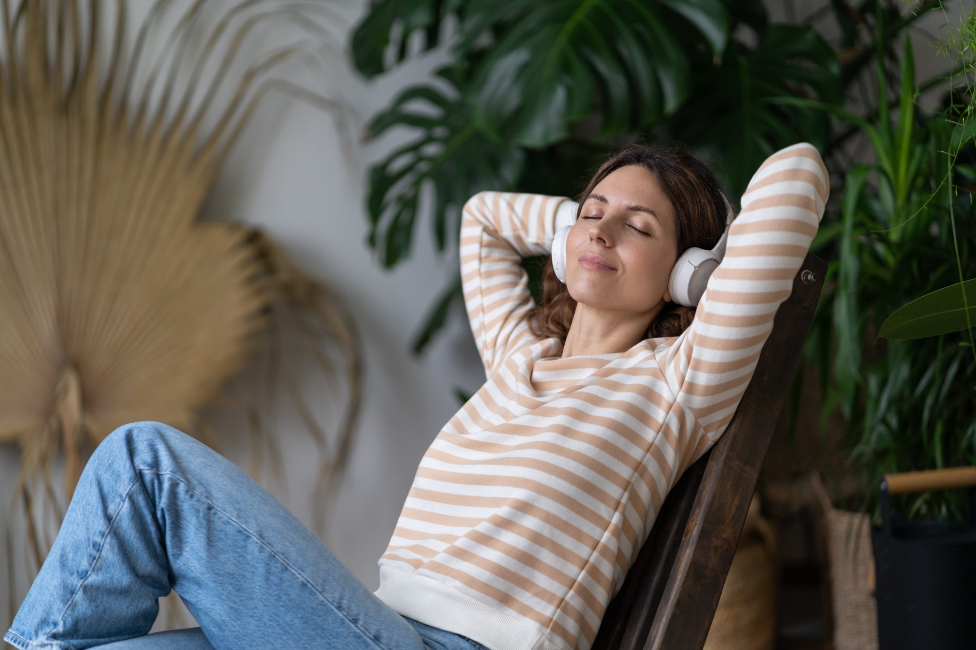 Woman relaxing on a break whilst working from home, listening to music, leaning back in chair, plants visible in background