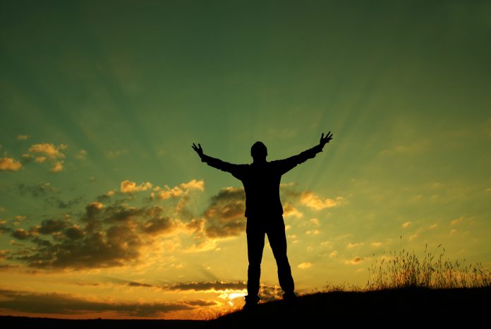 Silhouette of man with hands in air against a beautiful sunrise/sunset