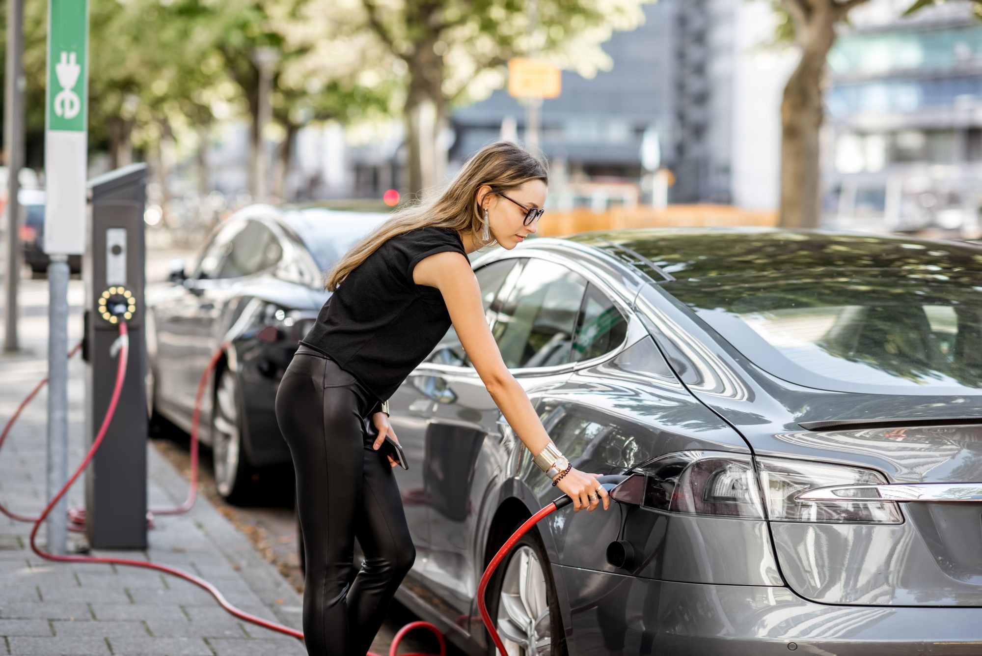 Caucasian woman dressed in black charges up her electric vehicle 