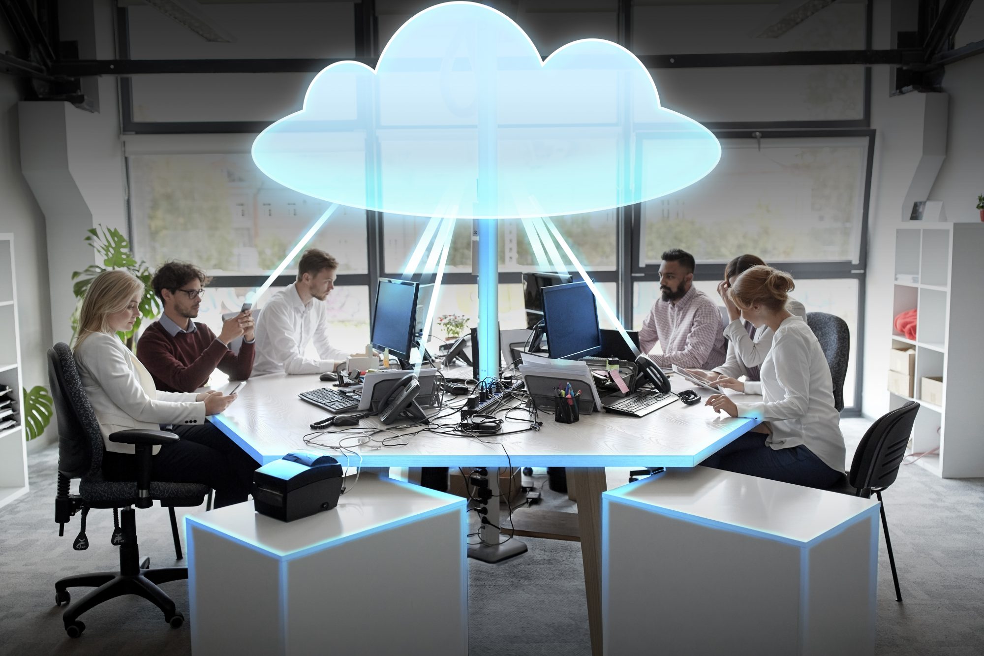 Office workers sitting round desk with cartoon cloud in middle of desk. Cloud concept 