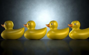 Four yellow rubber ducks sitting in a row against a dark blue green background