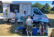 Van parked up on grassy area; adults and children sitting and standing around it participating in outreach event